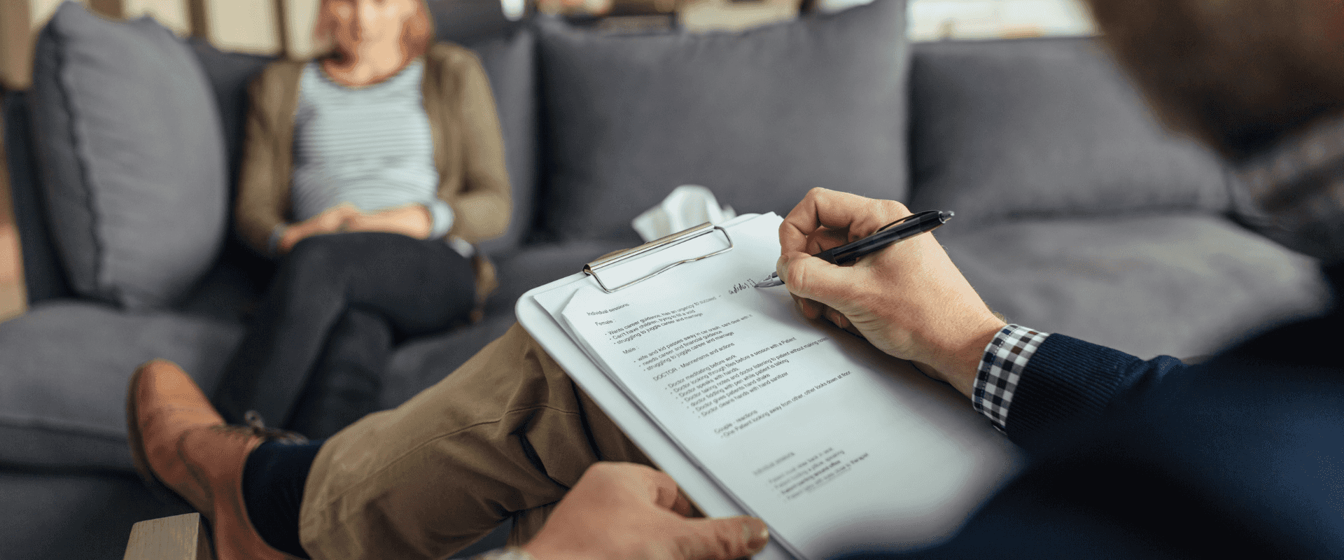 A male therapist sat with one leg crossed over the other in a chair opposite his client, a woman with her hands in her lap.